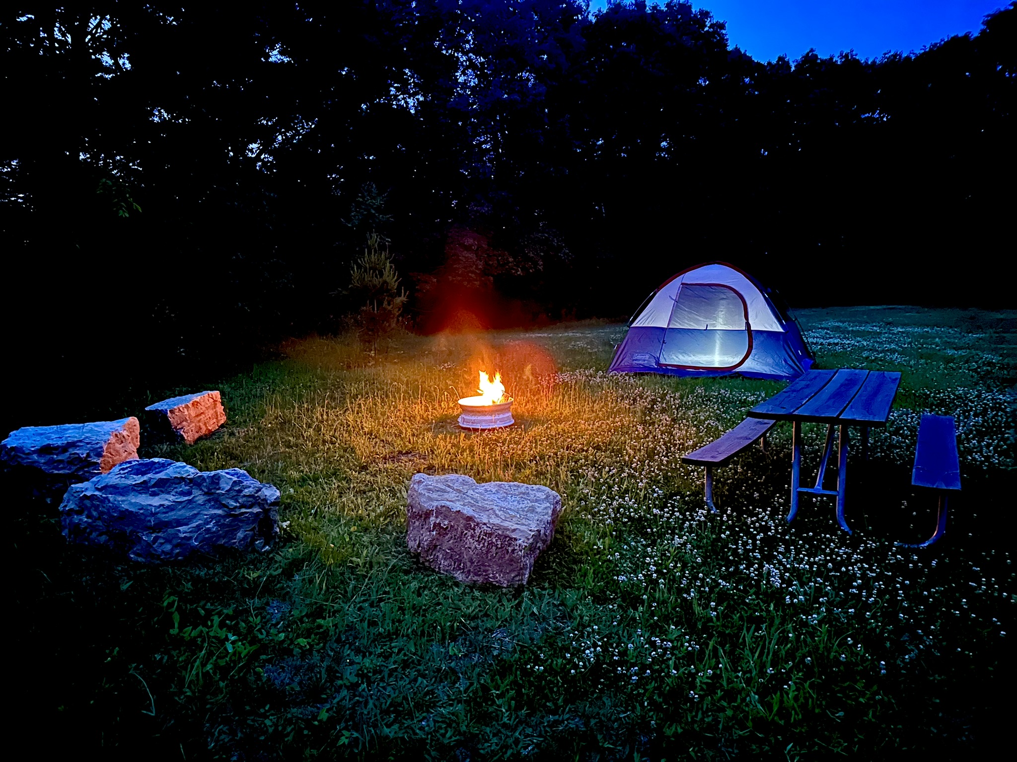 Fire ring with boulder seats by picnic table with tent at night in grass area