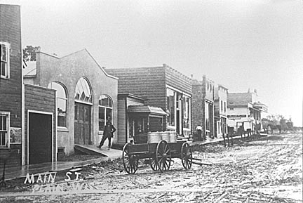 Plain: Main Street in early 1920's. L-R: Blacksmith Shop, Liegel Garage, Village Hall, Dr. P.H. Fowler's office, Post Office & I