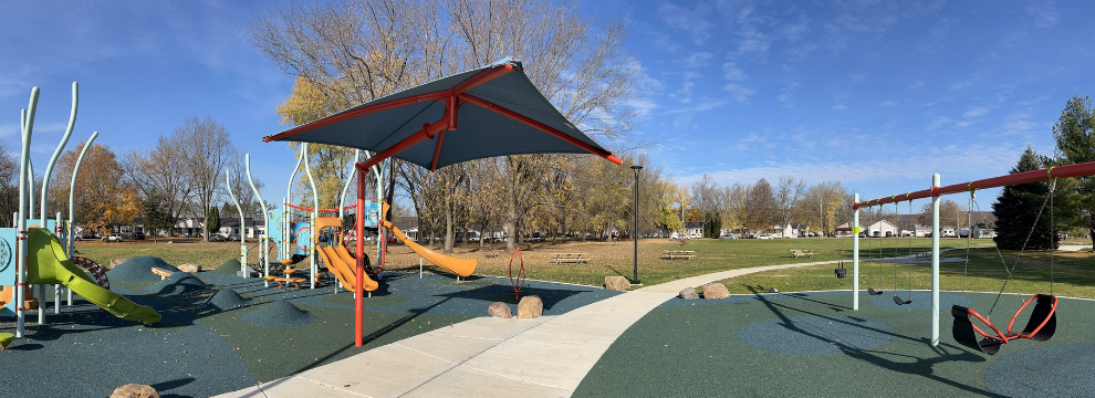 A photo of a playground, including a shade structure, swings and slides.