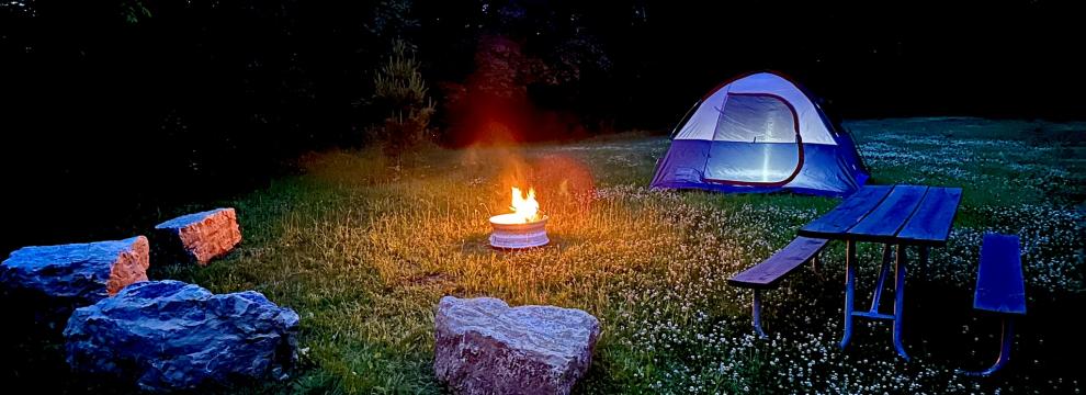 Fire ring with boulder seats by picnic table with tent at night in grass area