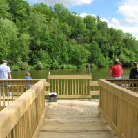 Four people stand on pier at the North End Boat Landing on Lake Redstone and look over the water while fishing