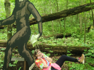 A woman gets pulled by her hat by a large Sasquatch cutout in the forest