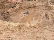 Monster truck toys scatted around a racetrack made of sand, with a pool of water in the center