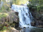 Recent, large waterfall flowing into an open pond surrounded by trees