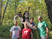 Large Sasquatch cutout in forest with 4 people smiling around it