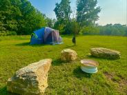 Rustic site 2 sits boulder seating surrounding a fire ring, with a tent in the background. 