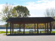Shelter covering a few picnic tables with lot in front and lake behind Shelter covering a few picnic tables with lot in front and lake behind