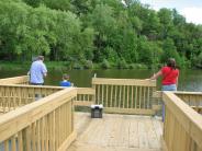 Three people stand on pier looking out over the water with fishing poles