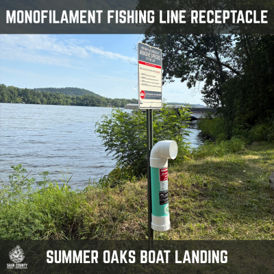 A monofilament fishing line receptacle is placed near the water at Summer Oaks boat landing, under invasive species sign
