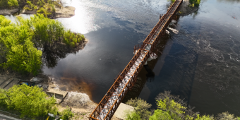 Great Sauk State Trail Update! A large truss bridge expanding over the Wisconsin River, also showing the shoreline with trees