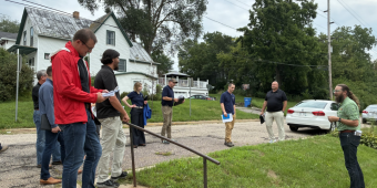 A group of 9 stand on a residential street while on a tour of the Baraboo Spur portion of the Great Sauk State Trail expansion