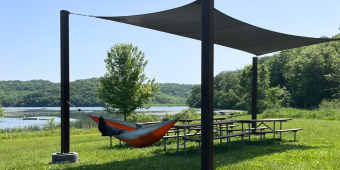 A person lays in a hammock attached to a shade structure, with their work boots poking out of the hammock