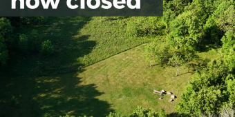 Rustic Sites Now Closed - 2026 Season Aerial view of a large mowed campsite in a forest, with a picnic table and boulder seats. Text - rustic sites now closed.
