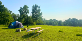 Photo of tent in wide open space near picnic table and fire ring to promote new rustic sites that are now open